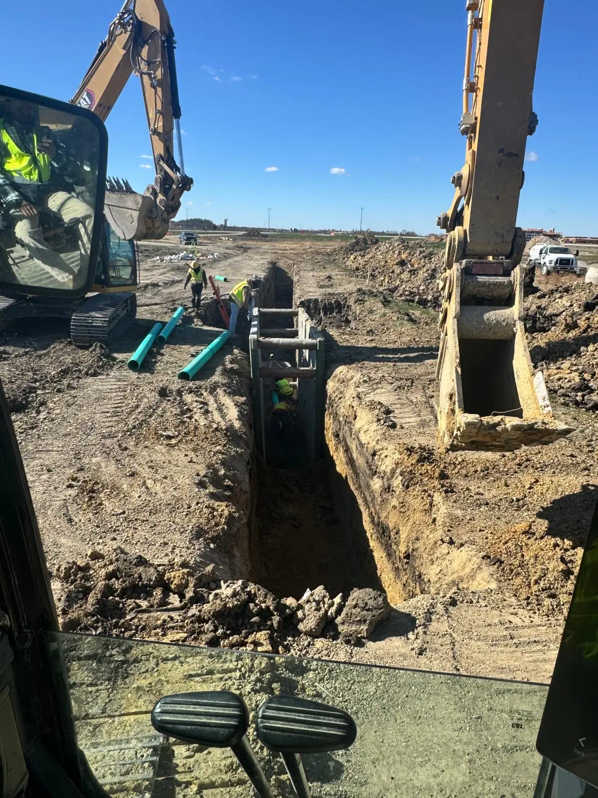 View from an excavator cab of a Castello Brothers crew working inside a trench box