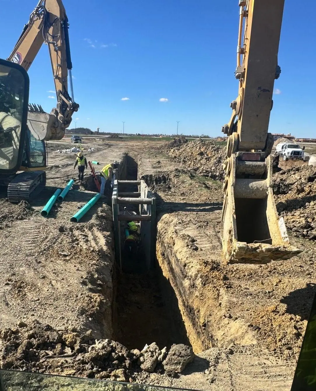 Castello Brothers excavators and crew installing sewer pipe inside a trench box