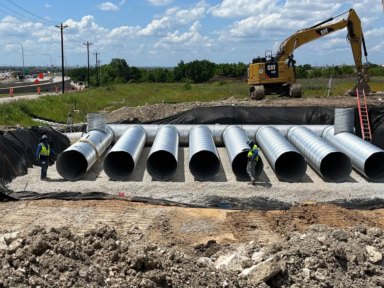 Castello Brothers Utilities crew installing large-diameter corrugated metal culverts beside a Dallas-Fort Worth highway