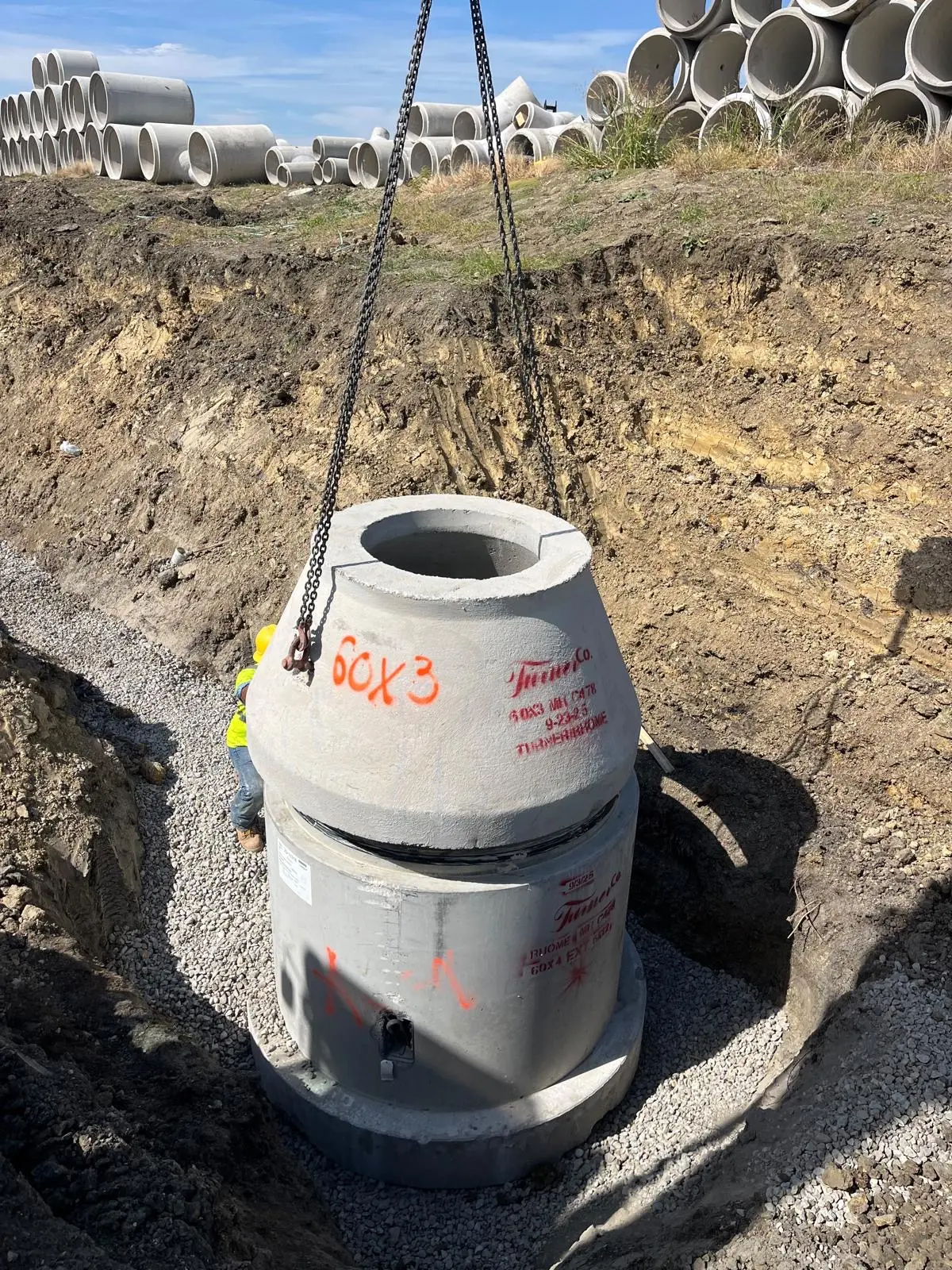 Precast concrete manhole cone section being set by crane in an excavation