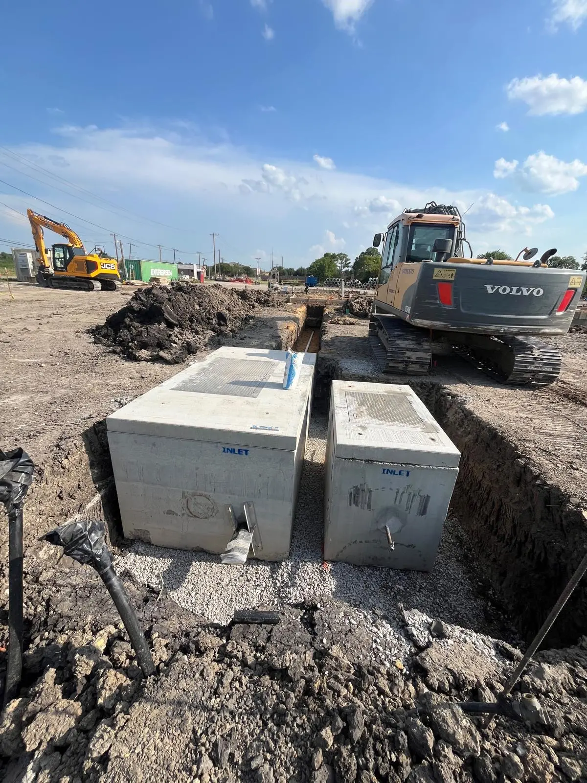Two precast concrete storm inlets set in place beside a Volvo excavator
