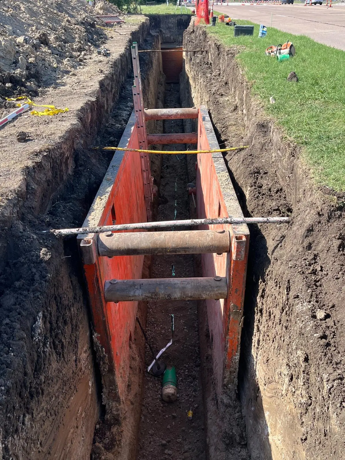 Orange trench shoring box in a deep utility excavation beside a road